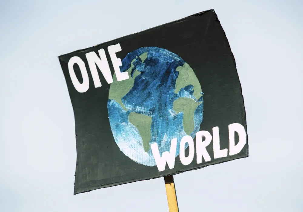 A sign with a handpainted picture of the globe with "ONE WORLD" written on top in white lettering