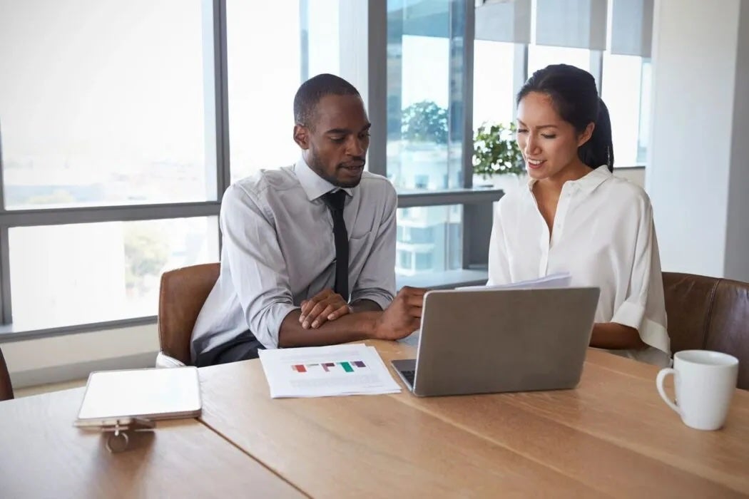Two people reviewing something on a laptop in a meeting room