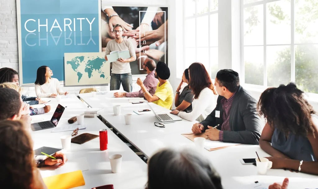 A board room meeting of people discussing charity as the topic with a map of the world at the head of the table
