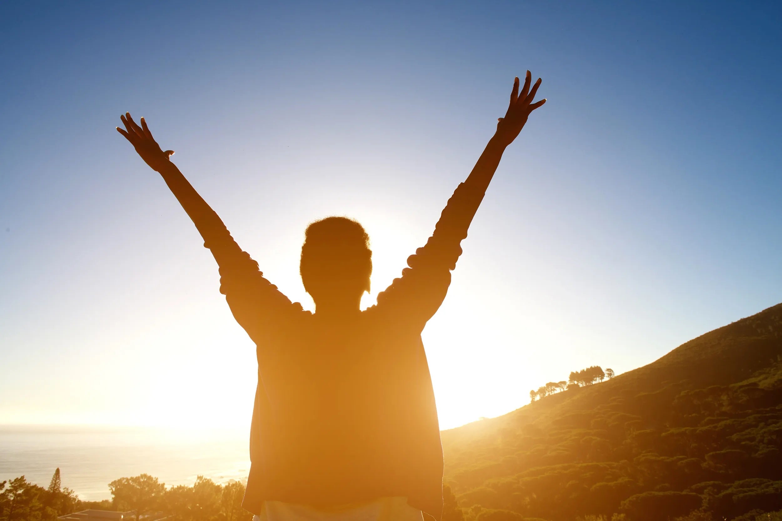 A person raising their arms up into the air as their silhouette cuts into the rising sun