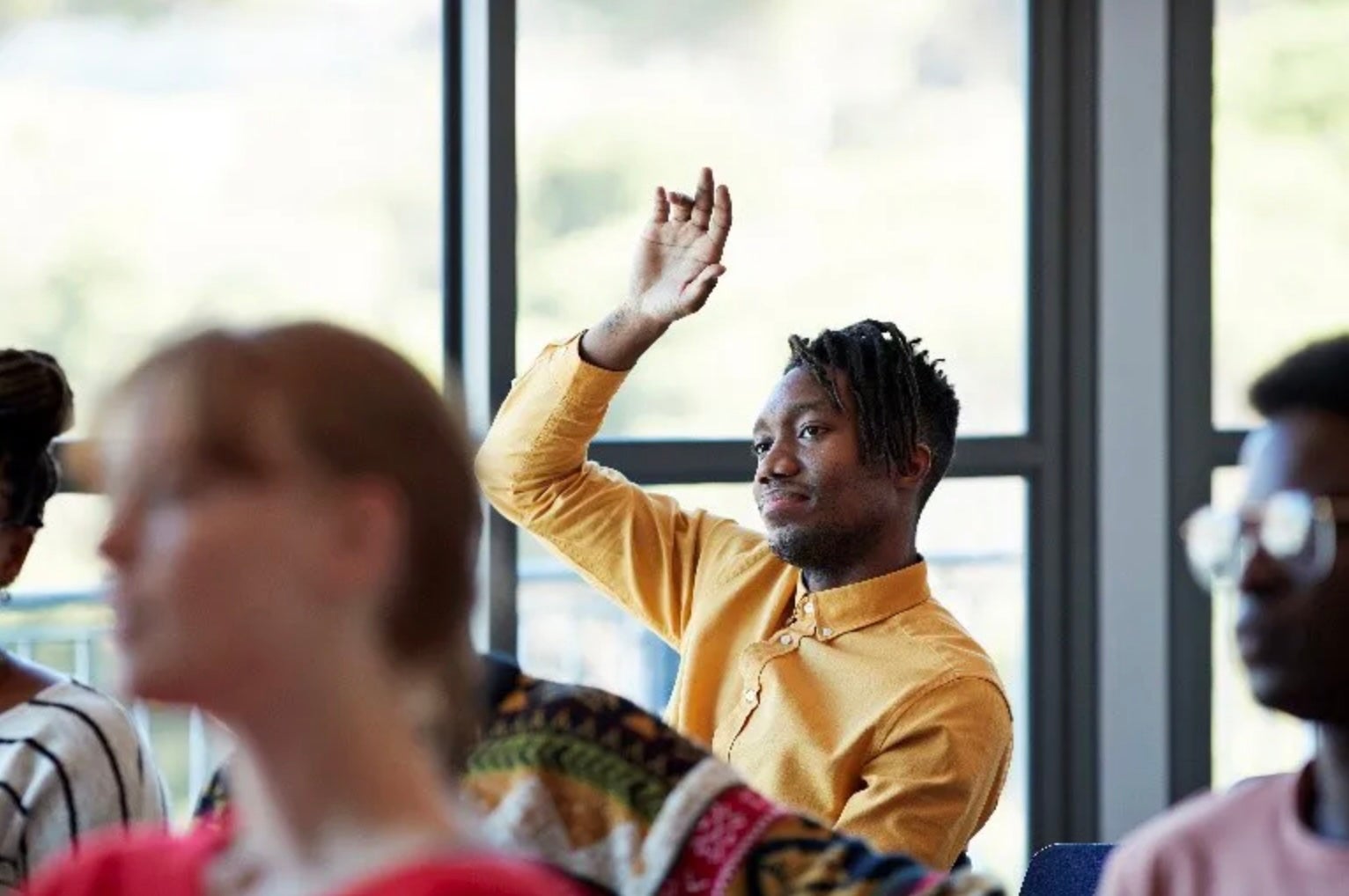 A man sitting in the back of a room raising his hand 
