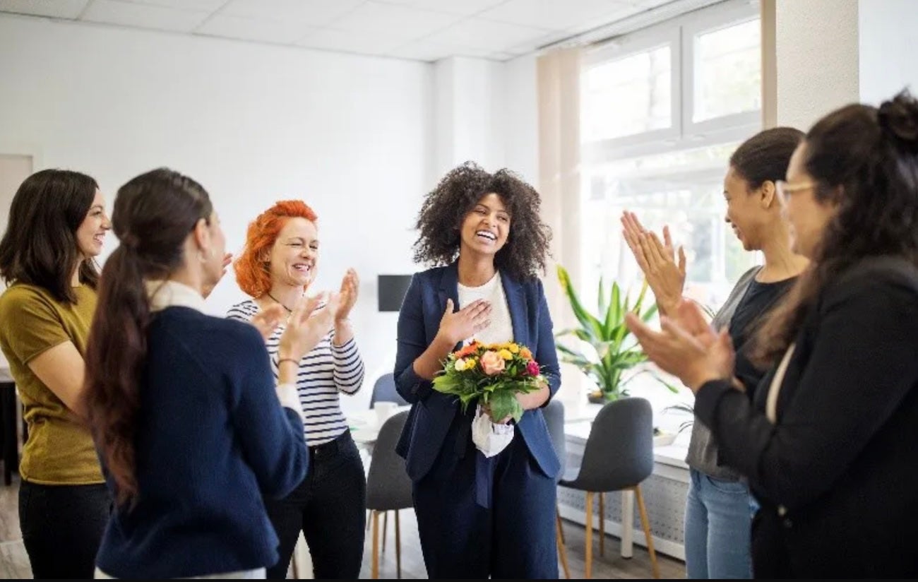 A group of women applauding for a woman in a blue suit with a bouquet of flowers